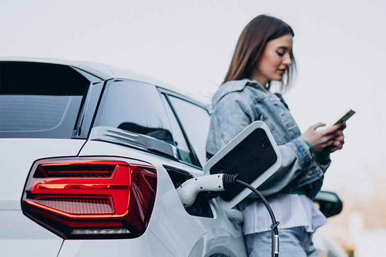Mujer cargando el coche el&eacute;ctrico con cargador port&aacute;til