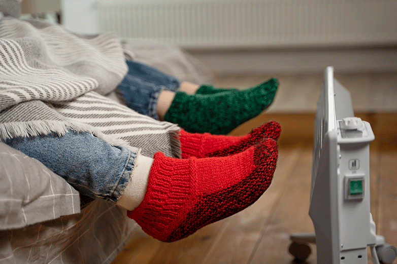 Dos personas calent&aacute;ndose los pies con un radiador
