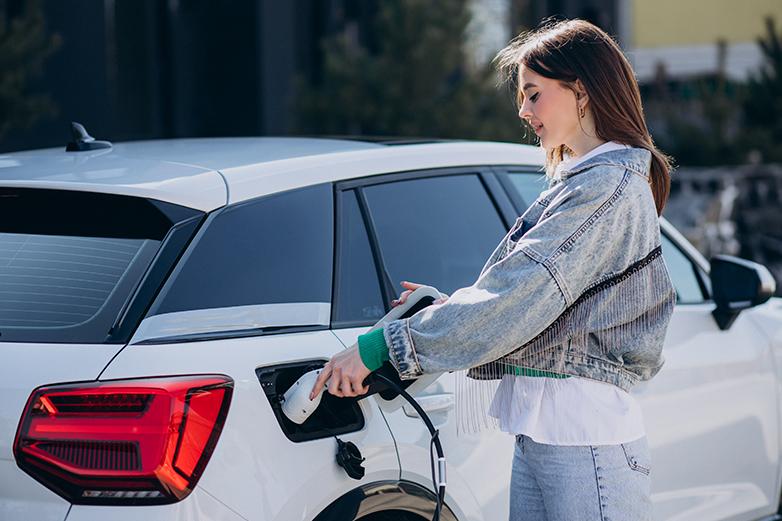 Mujer enchufando el cargador al coche el&eacute;ctrico