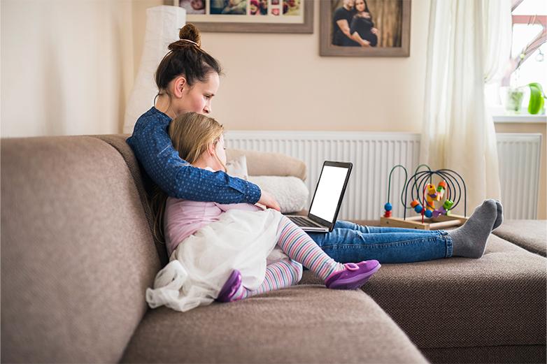 Mujer con su hija en el sof&aacute; viendo el port&aacute;til cerca del radiador