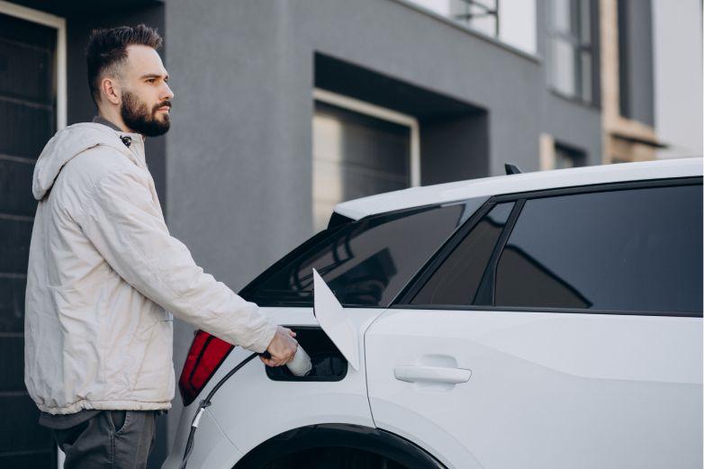 Hombre cargando el coche con el cargador el&eacute;ctrico frente a su casa