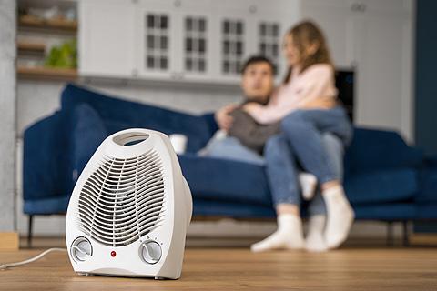 pareja en e sof&aacute; calentando el sal&oacute;n con un calefactor el&eacute;ctrico