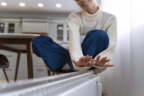 mujer calent&aacute;ndose las manos con el radiador el&eacute;ctrico