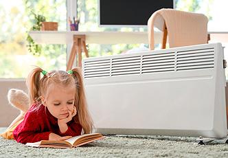 ni&ntilde;a leyendo junto a un radiador el&eacute;ctrico