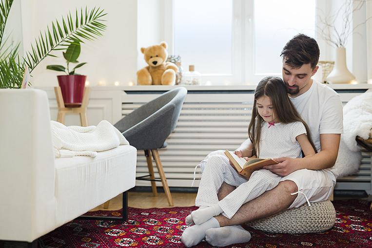 Padre e hija leyendo junto al radiador de su sal&oacute;n